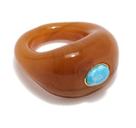 The Monument Ring by Lizzie Fortunato is a chunky brown resin cocktail ring with a round blue stone set in a small gold bezel—an eye-catching piece of wearable art.