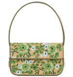 The Staud Tommy Beaded Bag showcases a curved strap and an intricate hand-beaded floral design with green and blue flowers on a woven tan background.
