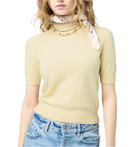 Woman wearing a light yellow Sweater Tee by Guest in Residence, blue jeans, a printed neck scarf, and a beaded necklace.