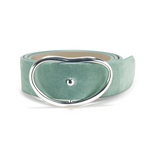 The Wide Georgia Suede Belt by Lizzie Fortunato, featuring aqua suede and a large, silver asymmetrical oval buckle, is shown rolled up against a plain white background.