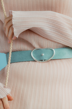 A person wears a ribbed, light pink long-sleeve top with thumb holes and a pale blue Wide Georgia Suede Belt by Lizzie Fortunato, holding a braided rope.