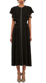 Someone wearing Ulla Johnson's Anais Dress in black, highlighted by ruffled sleeves and vertical stitching, paired with striped shoes for an ideal day-to-evening look.