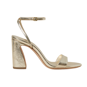 The Malia Curved Heel Sandal by Loeffler Randall is a gold, open-toe, high-heel sandal featuring a champagne leather texture and an adjustable ankle strap with a buckle.