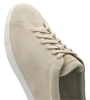 The Vantage Lite Suede Sneaker by Peter Millar displays a light beige suede upper with white stitching and a sleek white sole, featuring neatly tied laces.