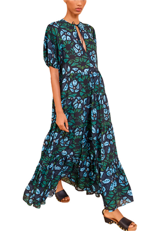 Wearing Ulla Johnson's Neera Coverup—a lightweight cotton blend dress with a green and blue leaf pattern, short sleeves, oversized fit, and front slit—the person pairs it beautifully with black platform sandals.