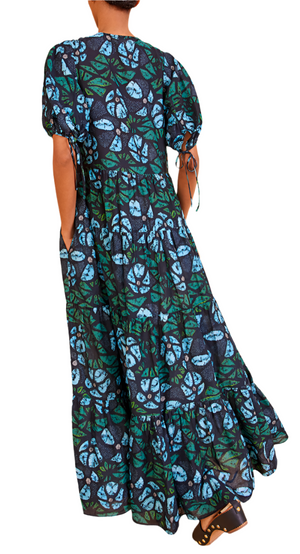 Wearing the Ulla Johnson Neera Coverup, featuring a lightweight cotton blend with blue and green leaf patterns, an oversized fit, short puffed sleeves, and pockets. The person is seen from behind in black sandals.