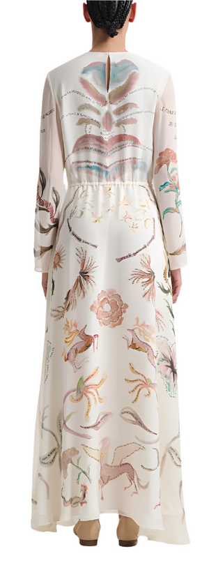 A woman is seen from behind wearing the Altuzarra Sybbeline Dress. This silk maxi dress, decorated with vibrant nature-themed illustrations of animals and flowers, drapes elegantly behind her.