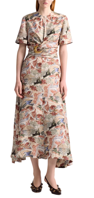 A person wearing the Altuzarra Honey Dress—a patterned, short-sleeve, ankle-length silk dress with a draped waist—paired with black heeled shoes featuring an oversized buckle.