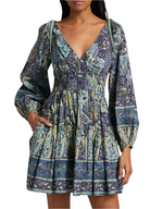 A woman wears the Ulla Johnson Anika Dress, a patchwork print mini dress with blouson sleeves, V-neckline, smocked waist, and pockets.