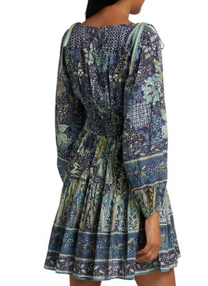 A woman is seen from behind wearing the Ulla Johnson Anika Dress, featuring a patchwork print, blouson sleeves, gathered waist, and shoulder tie details.