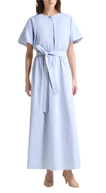 A woman wears the Paulina Banker Stripe Dress by Altuzarra—a light blue cotton poplin shirt dress with vertical stripes, short kimono sleeves, a tied waist belt—and beige heels.