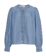 The Kady Blouse by Ulla Johnson is crafted from light blue water-washed cotton with geometric embroidery on the front, sleeves, and cuffs. It features a round neckline and front tassel ties.