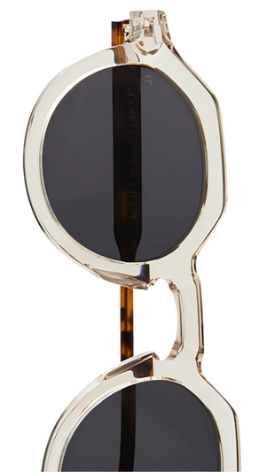Close-up of The Hometown round sunglasses by Jimmy Fairly, featuring a clear cellulose acetate frame and dark lenses, partially folded against a white background.
