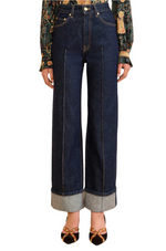 A person wears the Ulla Johnson Genevieve High Rise Jean, made from premium vintage indigo denim, styled with a patterned blouse and pointed-toe shoes featuring gold accents.