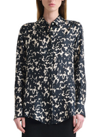 A woman wearing the Chika Top by Altuzarra—a relaxed, long-sleeve silk blouse with a black and white abstract spotted pattern and concealed buttons—stands against a plain background.
