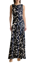 A woman stands against a white background wearing the Altuzarra Drina Dress—a sleeveless, floor-length silk gown with a black and white abstract pattern—paired with beige shoes.