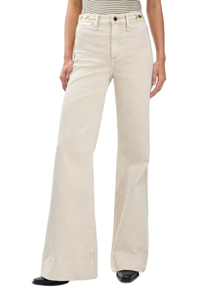 A person wears Rag & Bone Skylar High Rise Trouser Jeans in vintage stretch denim with a striped sleeveless top and black pointed shoes.
