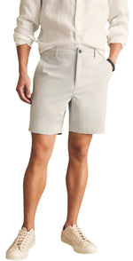 A person in a white shirt and Faherty's eco-friendly Belt Loop All Day Shorts, 7", stands with one hand in their pocket, wearing water-repellant white sneakers.