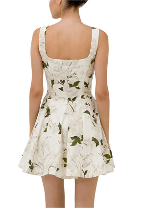 The woman is seen from the back wearing the Agua Dress by Agua By Aguabendita, a sleeveless white dress with a floral pattern, fitted bodice, and sweetheart neckline. Its flared skirt enhances her femininity, and her elegantly upstyled hair adds to the look.