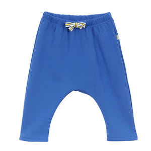 The Ferdinand Jogger by Arsene & Les Pipelettes features lightweight blue toddler pants made of soft cotton, an elastic waistband, and a charming small yellow and blue striped bow in front.