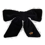 The Beaufort Bonnet Company’s T.B.B.C. x Lele Sadoughi Britney Barrette features black velvet, white lace trim, and a gold emblem, blending classic and elegant style reminiscent of Lele Sadoughi accessories.