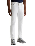 A person wearing AG Jeans' Tellis Modern Slim Pant in white, a dark shirt, and gray sneakers stands against a plain background.