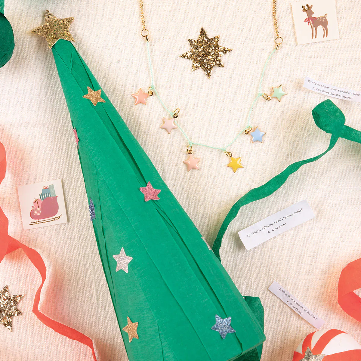 The Meri Meri Surprise Christmas Tree includes a festive cone hat, star necklace, streamers, holiday cards, and gold star ornaments—ideal as a holiday gift—beautifully displayed on a light background.
