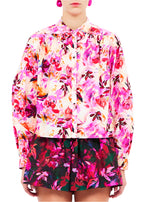 Someone wearing Ulla Johnson's Tahlia Blouse and matching shorts, crafted from 100% cotton with vibrant floral prints in bright pinks, reds, and purples.