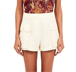 A person wearing Ulla Johnson's Sadie Short in cream cotton Tencel with buttoned pockets and a red patterned top.
