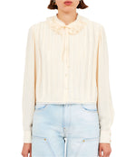 A person is wearing the Ulla Johnson Karla Blouse, a luxurious silk button-up in light cream with a frilled collar, paired perfectly with light blue jeans.