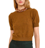 A woman wears the Ulla Johnson Liv Embroidered Cashmere Knit in umber brown with short sleeves, dark pants, and a chunky beaded collar.