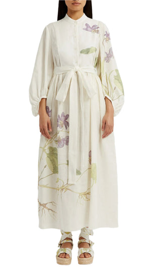 A person wearing the Erdem Long Sleeve Midi Dress With Tie Waist Detail featuring a white linen fabric, light green and purple botanical prints, balloon sleeves, and platform sandals.