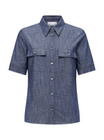 The Vesper Top by Callas Milano is a short-sleeved, button-up denim shirt with a collar and two front pockets, all in a rich Indigo color that exudes retro appeal.