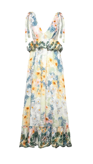 The Infinito Maxi Dress by Agua By Aguabendita features a sleeveless floral design with ruffled waist and hem. It boasts yellow, orange, blue, and green shades on white, accentuated by striking bows for elegance.