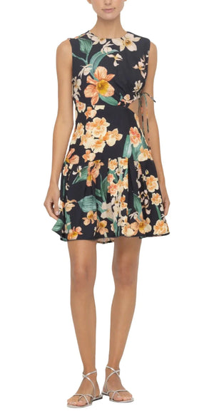 Person wearing the bestselling Agua By Aguabendita 'Otono Mini Dress,' a sleeveless black piece adorned with an orange and white floral pattern, standing with hands by sides in strappy sandals. Crafted from recycled viscose, it merges style with eco-friendly fashion.