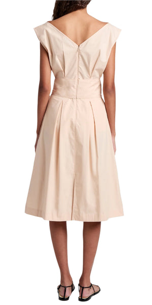 The Proenza Schouler White Label Caro Dress Brushed Poplin showcases an A-line silhouette with a self-tie waist belt, beige knee-length design, cap sleeves, and a pleated skirt. The woman in the dress stands with her back to the camera, highlighting black sandals.