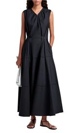A woman wears the Proenza Schouler White Label Kailey Dress Stretch Poplin, a sleeveless, ankle-length pleated fit-and-flare style, paired with a white clutch and black sandals.