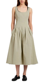 A woman wears the Proenza Schouler White Label Shelby Dress, a sleeveless light beige fit-and-flare midi cotton dress with a square neckline and pleated skirt, paired with black slip-on shoes.