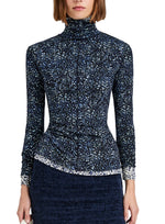 A woman wears the Proenza Schouler White Label Audrey Cheetah Jersey Top, a long-sleeve, turtleneck style with a subtle blue and white pattern, paired with a textured dark skirt. The image is cropped at the shoulders and thighs.