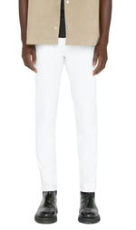 A person in a beige jacket, black shirt, and Frame's L'Homme Slim Denim in Whisper White with black boots stands against a plain background.