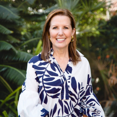 Photo of Sara McCann wearing a blue and white floral dress in front of tropical foliage