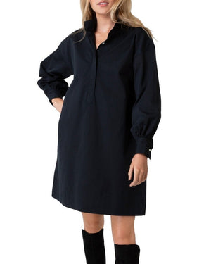 A person in an Ann Mashburn Anaya Popover Dress, a black collared shirt dress with long puffed cotton poplin sleeves, styled with knee-high black boots, stands against a white background.
