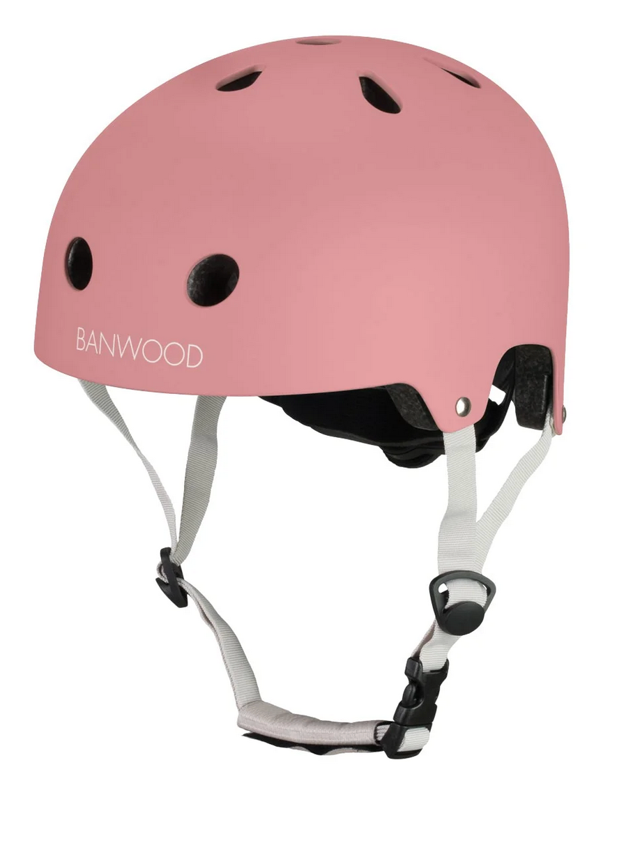 The Banwood Eco Helmet in pink features ventilation holes, adjustable white straps, and a black buckle, displayed on a white background.