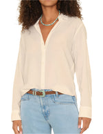 A person wears the Xirena Beau Shirt by Xirena, a white cotton poplin button-down, tucked into light blue jeans with a brown belt and a turquoise beaded necklace.