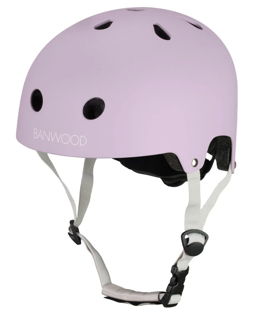 A Banwood Eco Helmet in light purple, featuring ventilation holes, white adjustable straps, and a black buckle, is displayed against a plain background.