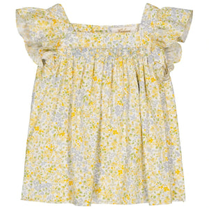 The Girls' Dianella Smocked Blouse by Kidiwi is a loose-fitting, short-sleeved piece featuring a floral pattern with ruffled shoulders and a square neckline. It has exquisite hand-embroidered details in yellow, green, and pale blue on a white background.