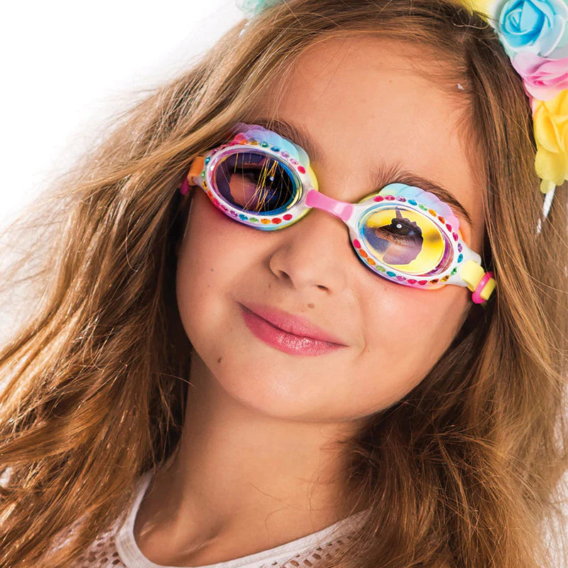 A young girl with long brown hair, wearing Bling2O's Eunice the Unicorn Swim Goggles and a floral headband, smiles at the camera.