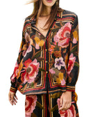 A woman wears the Farm Rio FR Chenille Flowers Black Shirt, a dark long-sleeved top with bold florals and geometric stripes, made from eco-conscious viscose and paired with matching pants.