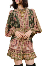 A woman wears the Farm Rio Flowering Garden Tree Green Mini Dress, featuring green florals, long puff sleeves, and pink and beige stripes, styled with a gold necklace and belt—the ideal chic look for a garden party.