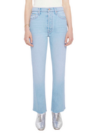A person wears Mother’s The Tripper Flood Fray light blue high-rise flare jeans, a white top, and silver ankle boots, standing against a plain white background.